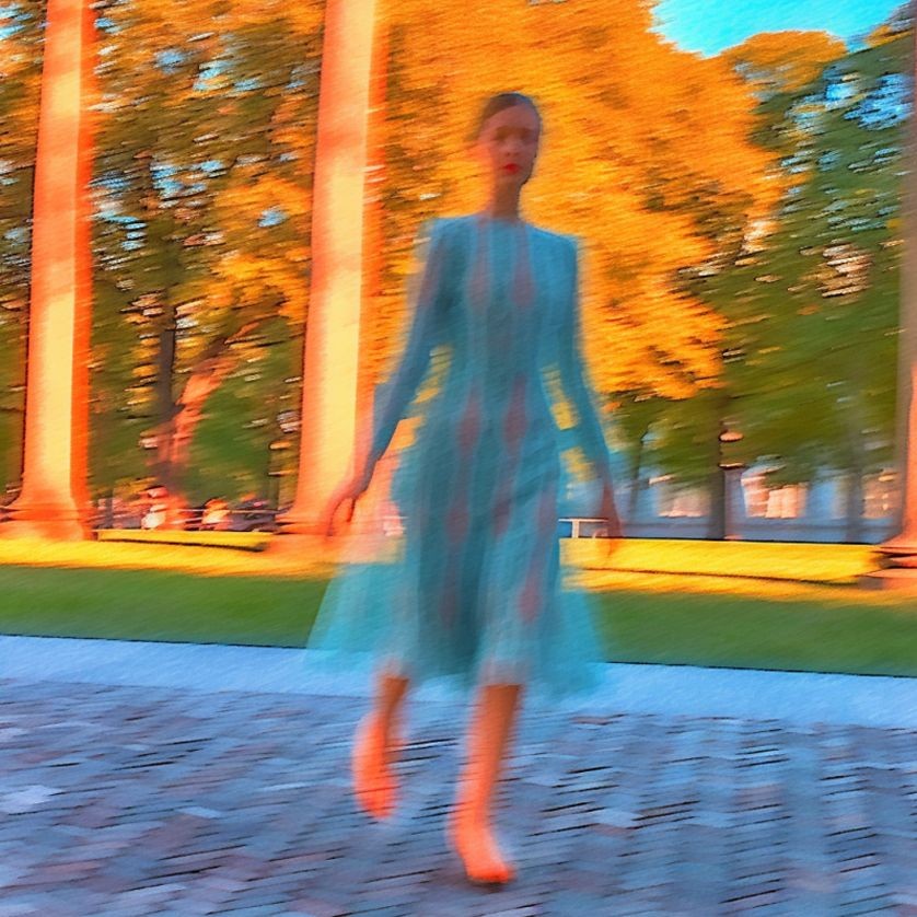 Blurred image of a person walking in a park with tall trees and sunlight in the background.